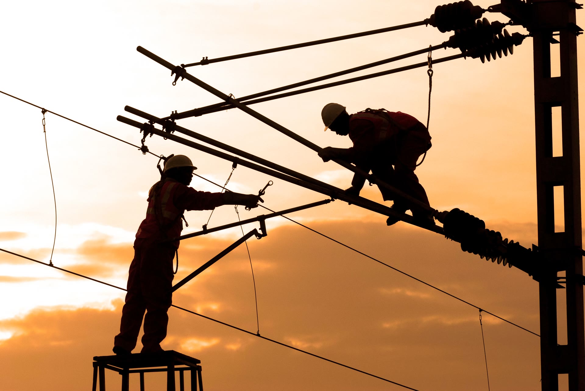 Two linemen working on a power line at sunset